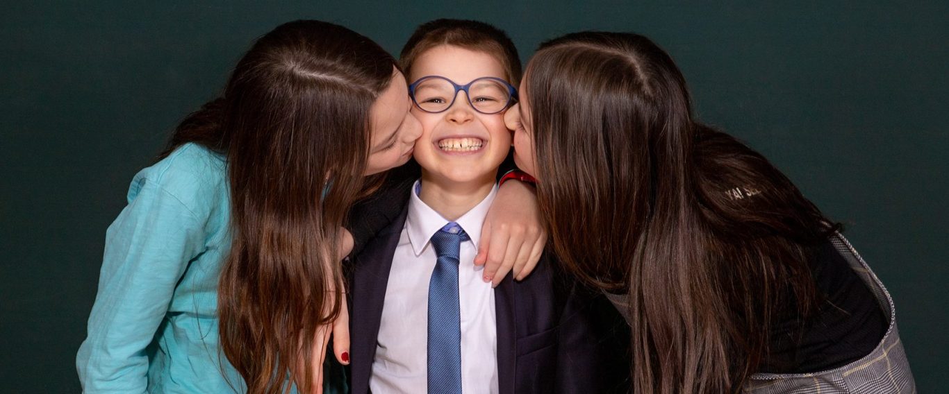 Ein kleiner Junge freut sich, weil er von seinen Schwestern geküsst wird