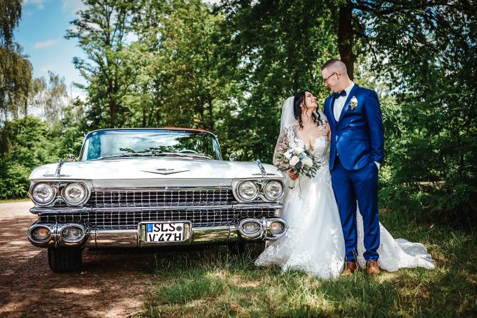 Braut und Bräutigam umarmen sich vor einem eleganten Auto