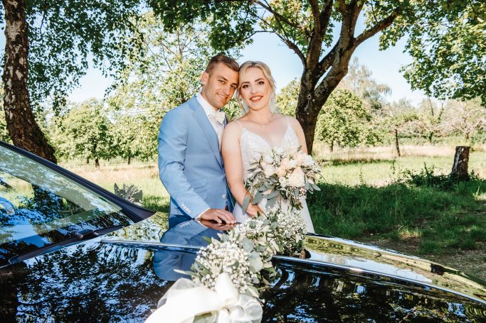 Braut und Bräutigam umarmen sich vor einem eleganten Auto